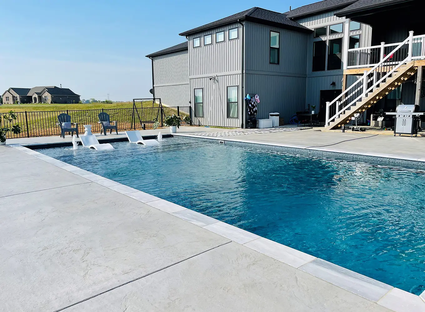 Modern rectangular pool with built-in water features and concrete pool deck at an Edwardsville IL residential home.