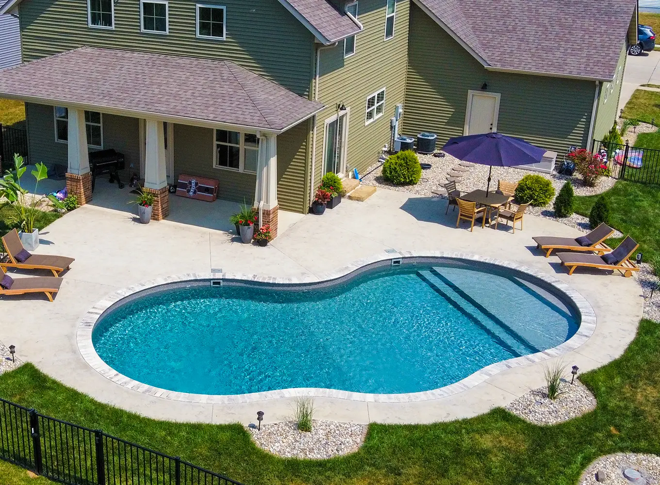 Aerial view of a freeform vinyl liner swimming pool with curved concrete deck behind a Midwest residential home in Shiloh IL.