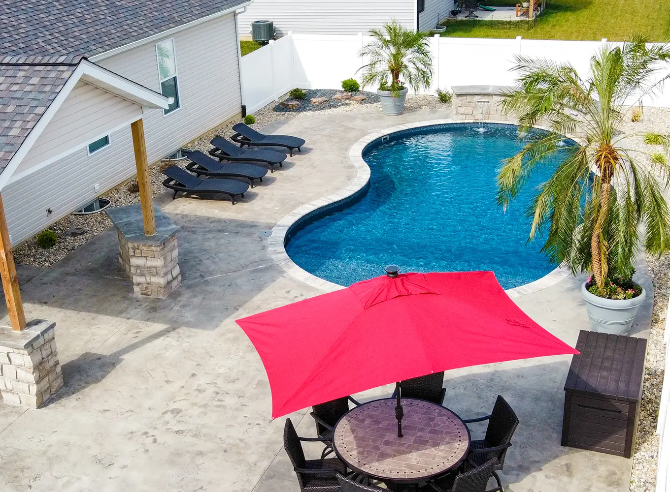 Freeform vinyl liner pool with palm planters, concrete deck, and outdoor seating at a Shiloh IL home.