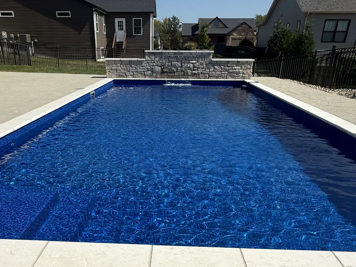 Rectangular fiberglass swimming pool with deep blue water and stone water feature in a suburban Troy IL backyard.